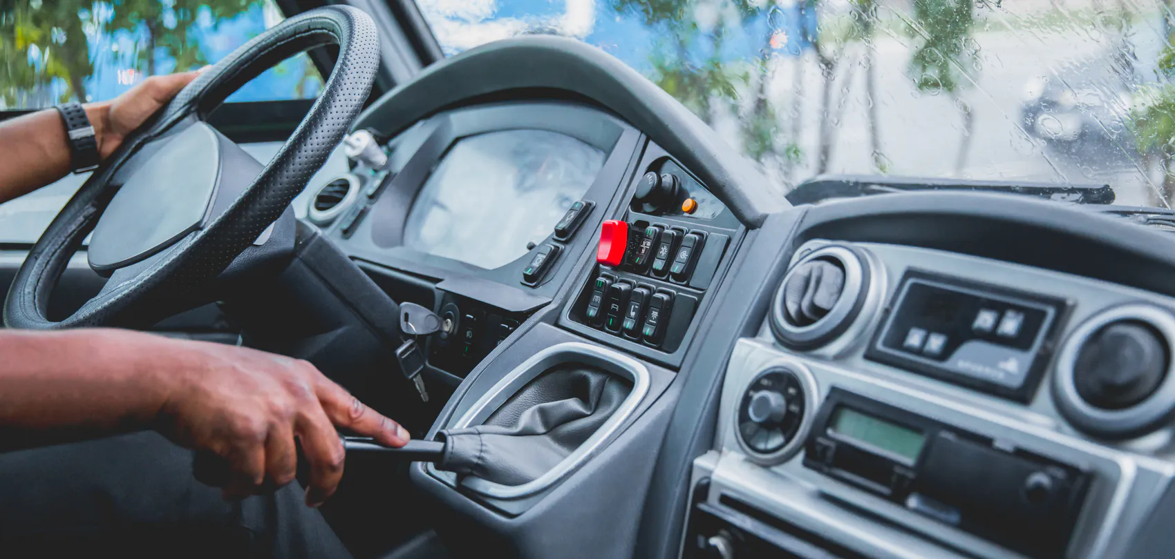 Buschauffeur met de handen aan het stuur en de versnellingspook van een bus: rijles voor het busrijbewijs