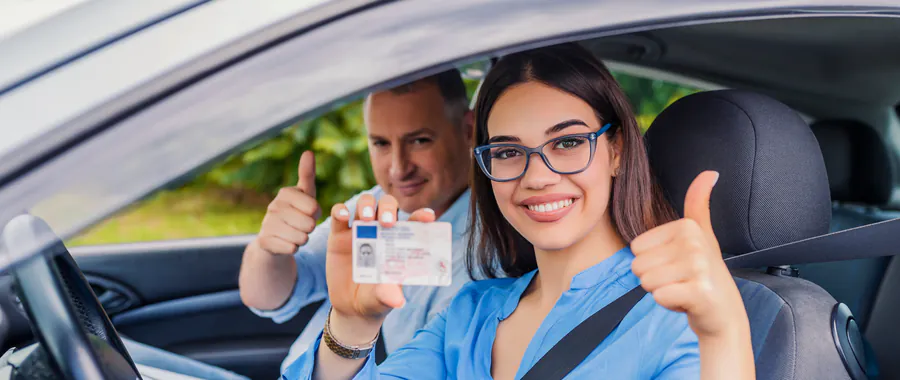 Geslaagde leerling toont haar rijbewijs en steekt met de rij-instructeur haar duim op in de lesauto