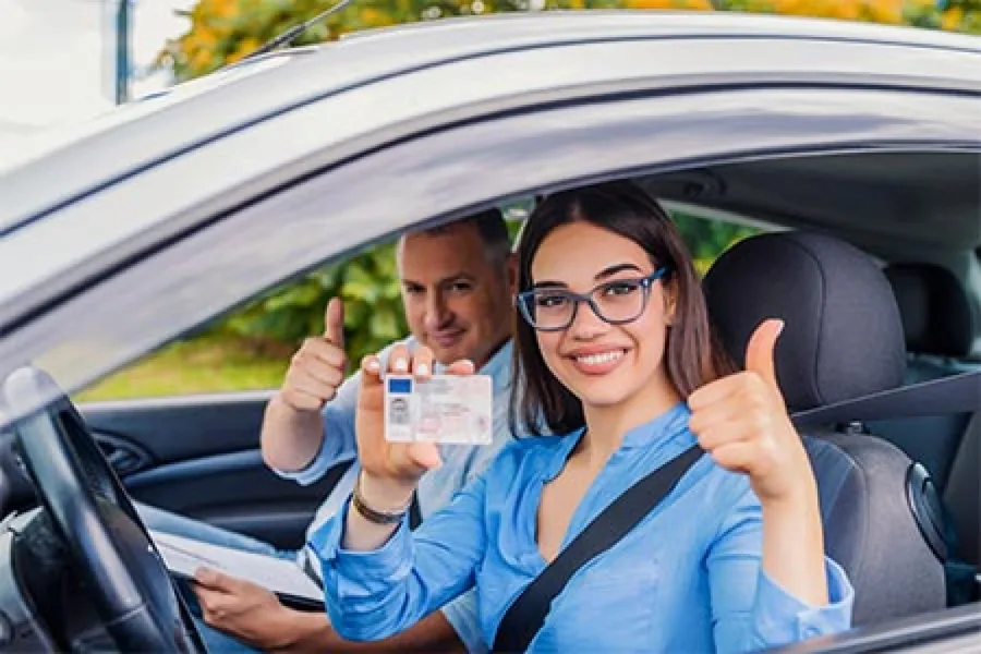 Geslaagde leerling met rijbewijs en instructeur steken hun duim op in de lesauto