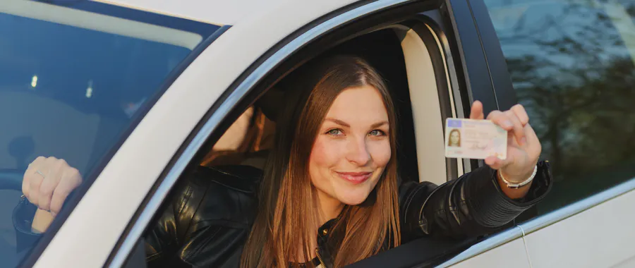 Jonge vrouw laat vanuit de auto trots haar nieuwe rijbewijs zien