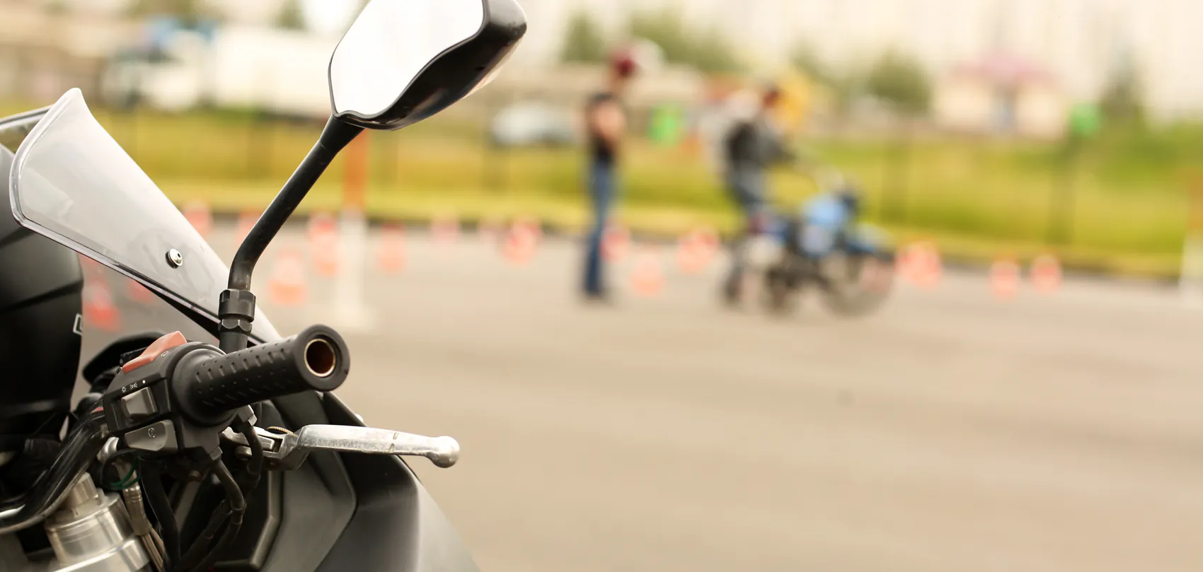 Stuur van een motor op het oefenterrein van een motorrijschool, met pionnen en een leerling op de motor