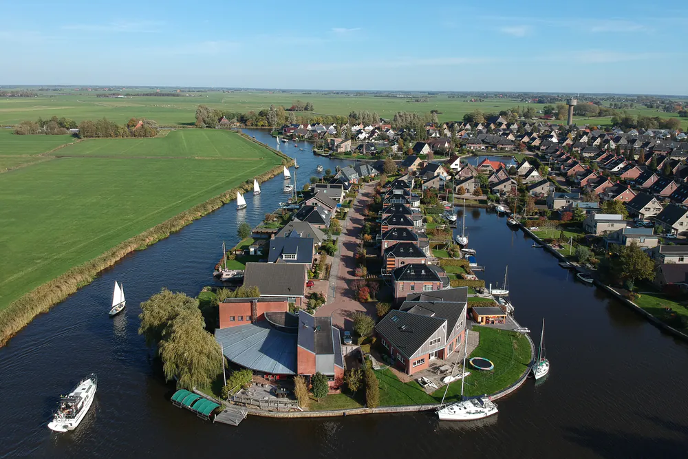 Luchtfoto van Akkrum met woningen en bootjes aan het water: vergelijk de rijscholen in Akkrum