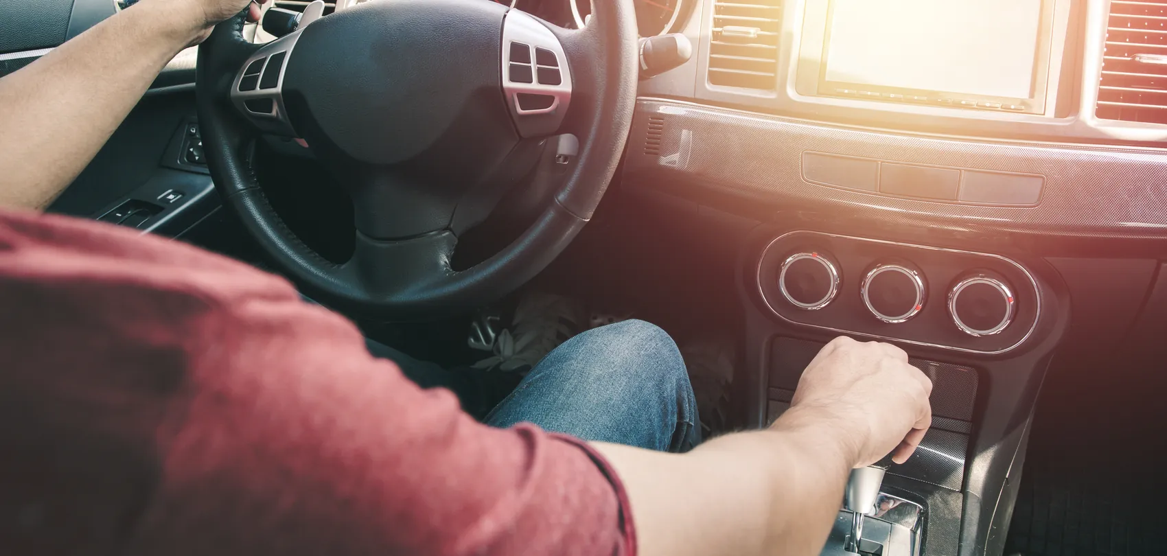 Bestuurder met één hand aan het stuur en de andere op de pook van een automaat: rijles in een automaat