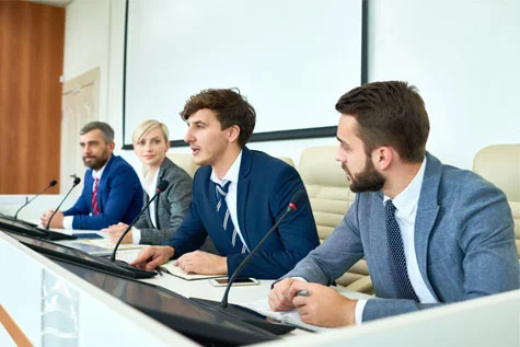 Vier mensen in pak aan een tafel met microfoons tijdens een persconferentie