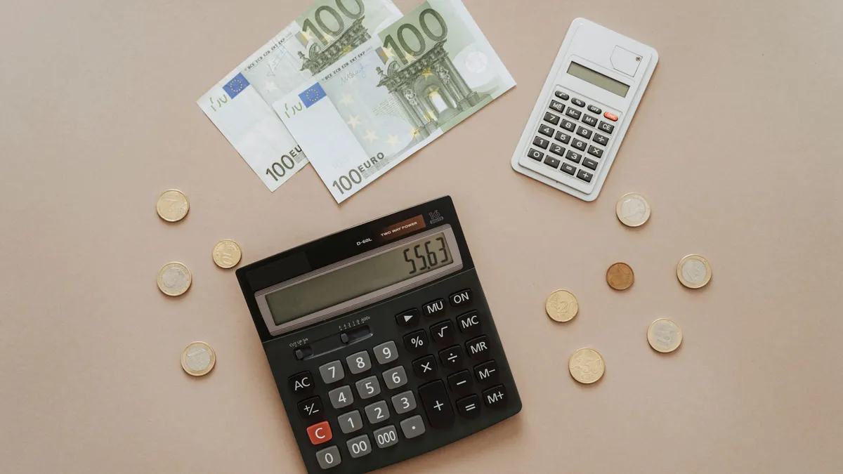 Twee rekenmachines, euromunten en briefjes van honderd euro op een beige tafel